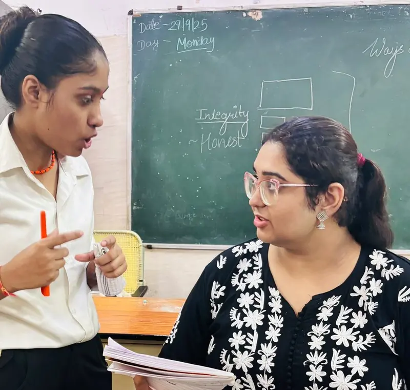 A TalkTheTalk teacher in conversation with a student in front of a chalkboard