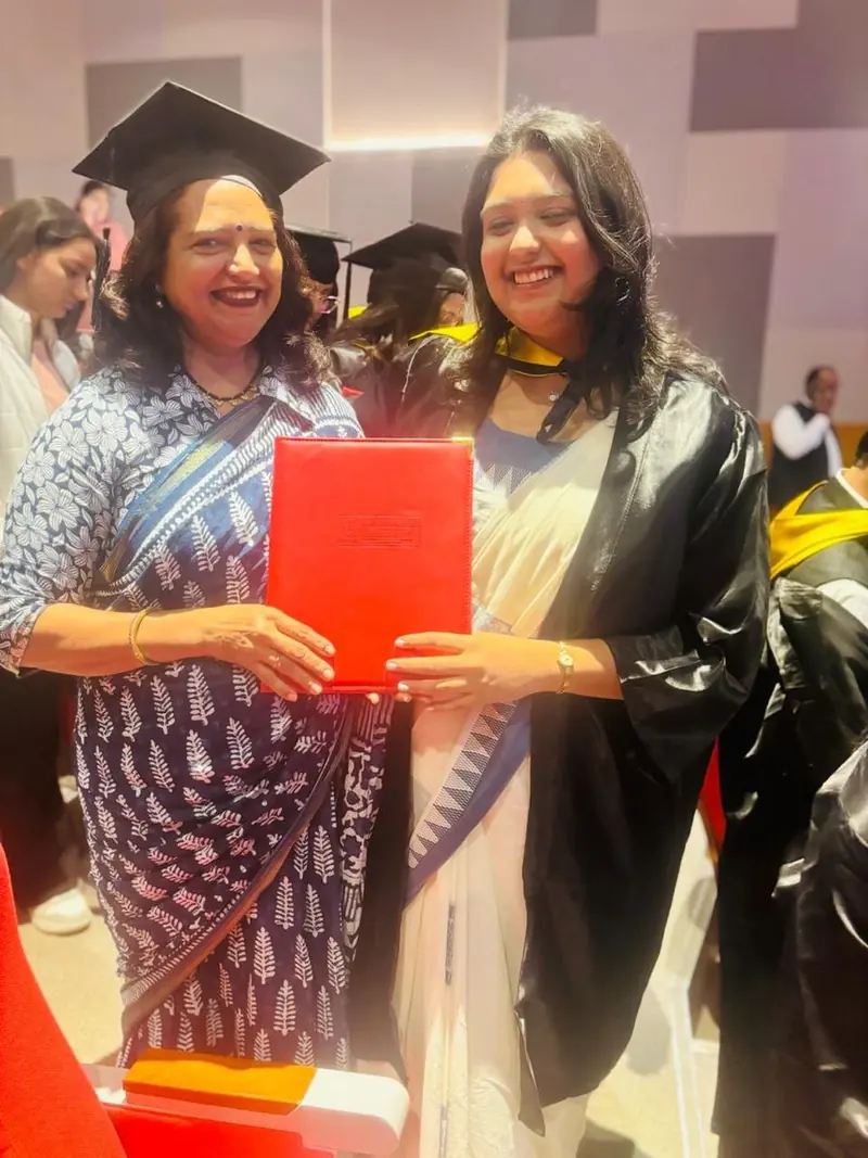 Two women in academic gowns at a convocation, holding a red folder